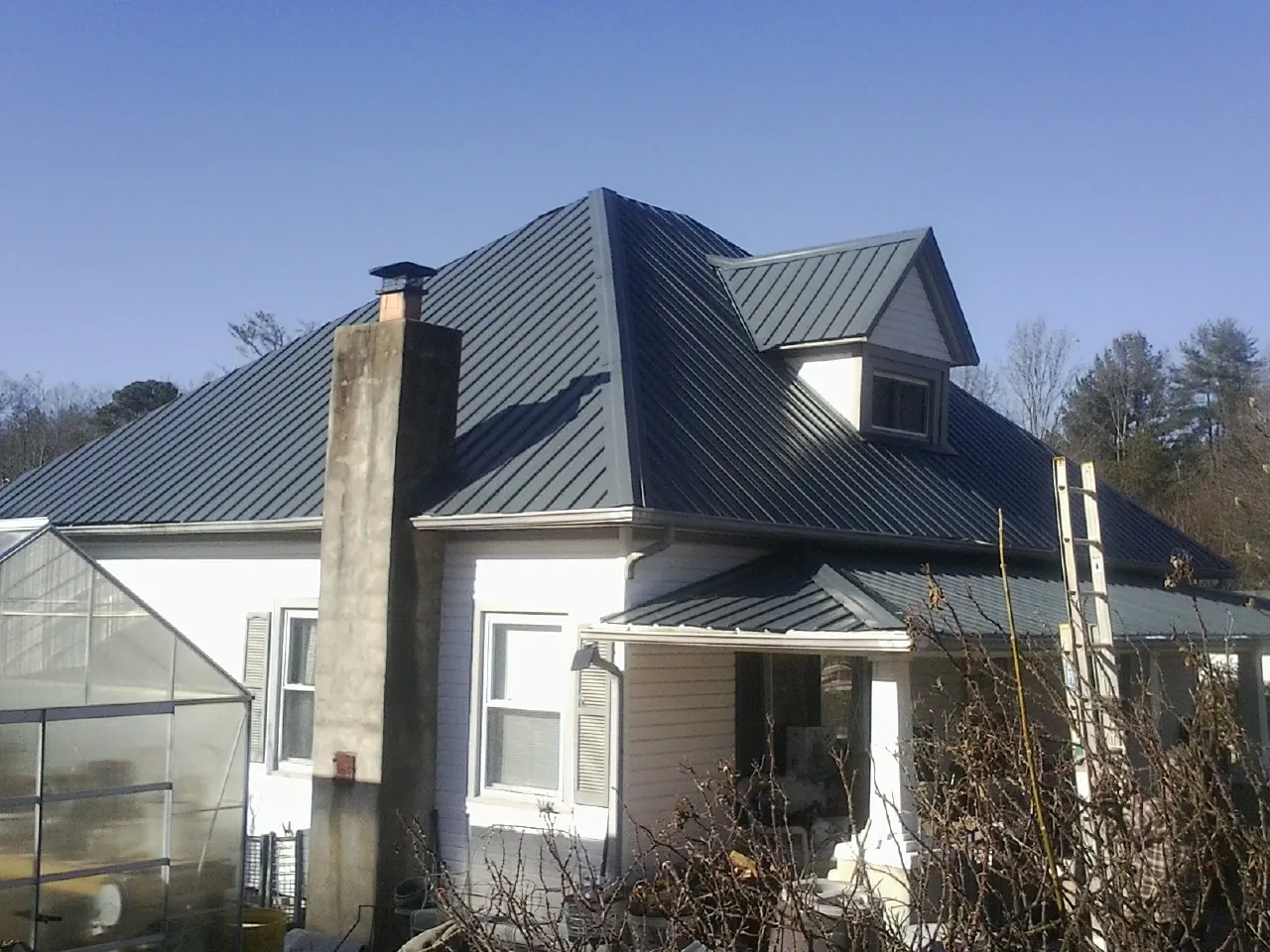 Dark blue standing seam metal roof on a white farmhouse with dormer — Slate & Tile Roof Repair by Roofing Brothers in Gambell