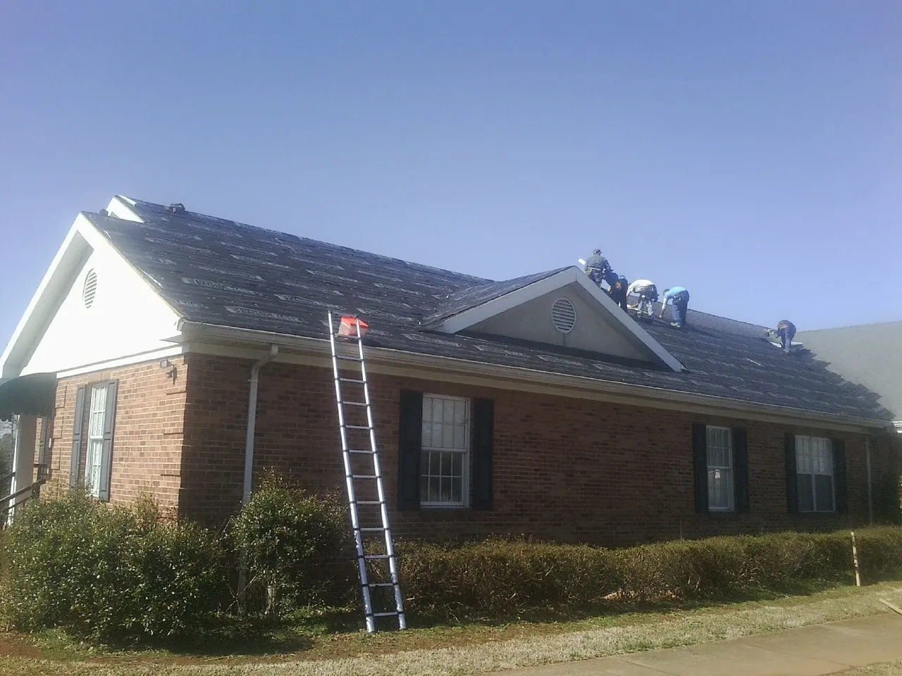 Crew tearing shingles off a brick ranch roof with a ladder set — Metal Roof Repair work by our crew in Gambell