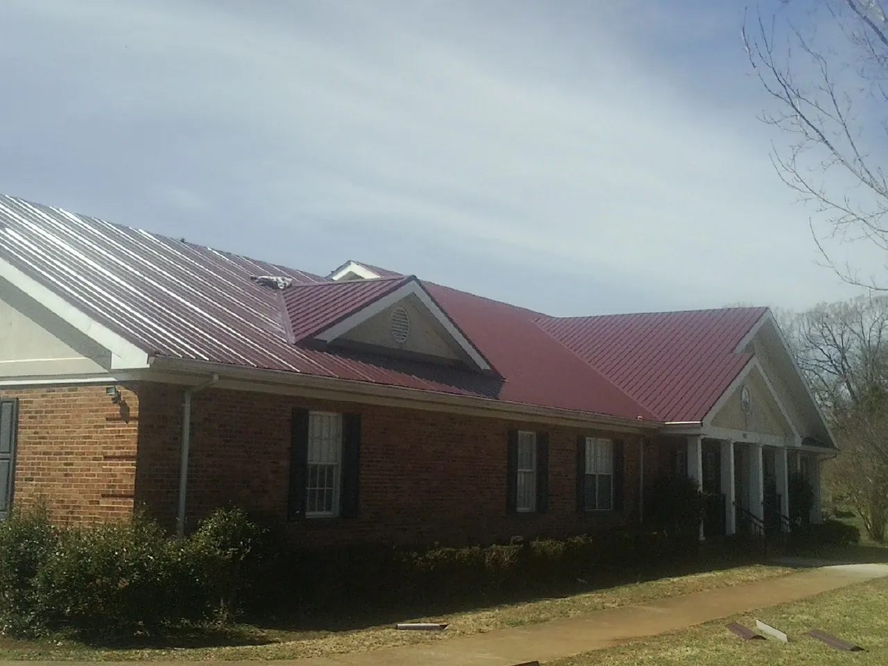 Red metal roof with gabled entries on a long brick building, from a Hail Damage Roof Repair job in Gambell