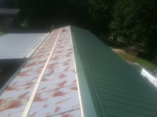 Old rusted panels beside newly installed green metal roofing — Wind Damage Roof Repair by Roofing Brothers in Gambell