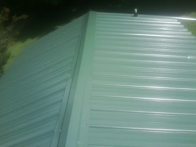 New green metal panels meeting at the ridge of a roof — Flat Roof Repair work by our crew in Gambell
