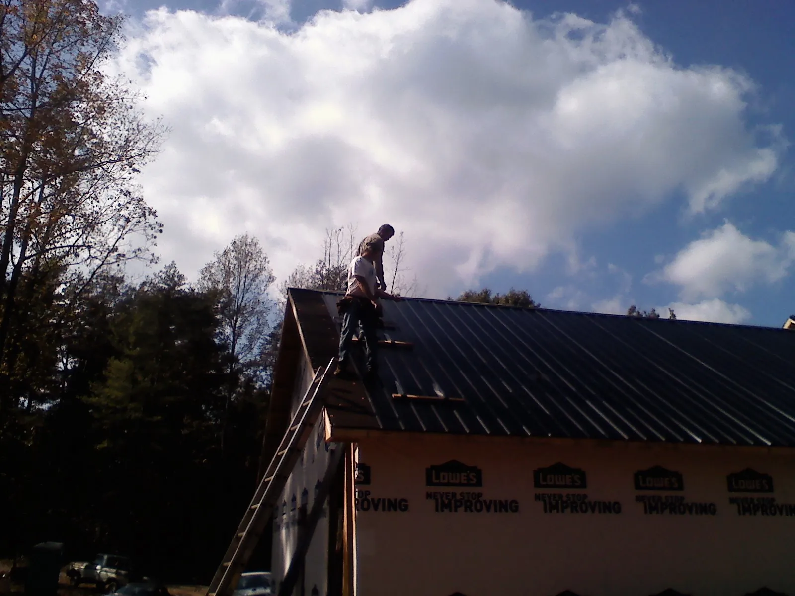 Roofer fastening dark metal panels high against a cloudy sky, from a Roof Inspection job in Gambell