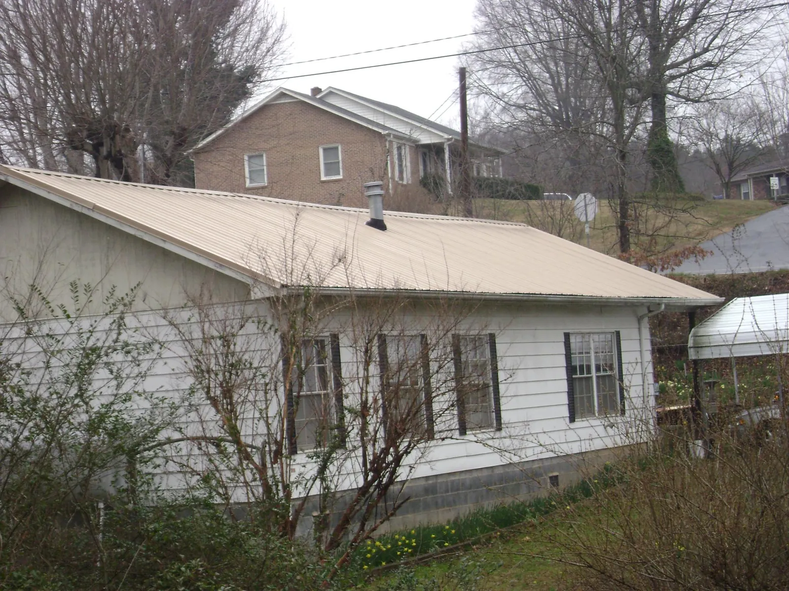 Tan metal roof on a white sided house set into a hillside — Commercial Roofing by Roofing Brothers in Gambell
