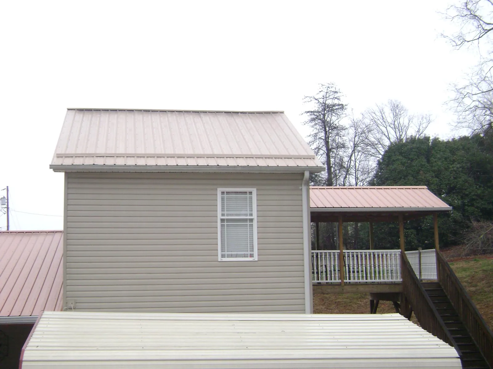 Tan metal roofs on a two story addition and attached porch, from a Roof Replacement job in Gambell